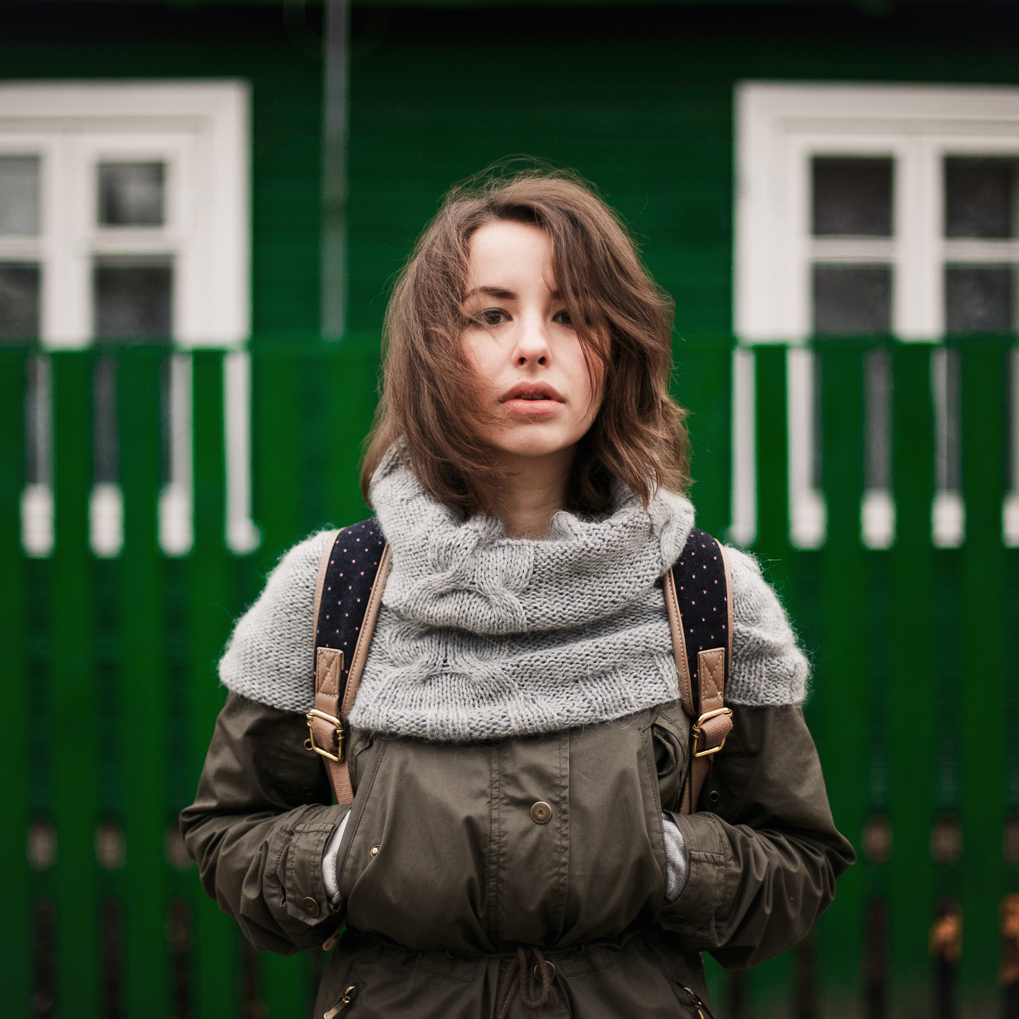 young woman in coat with green fence