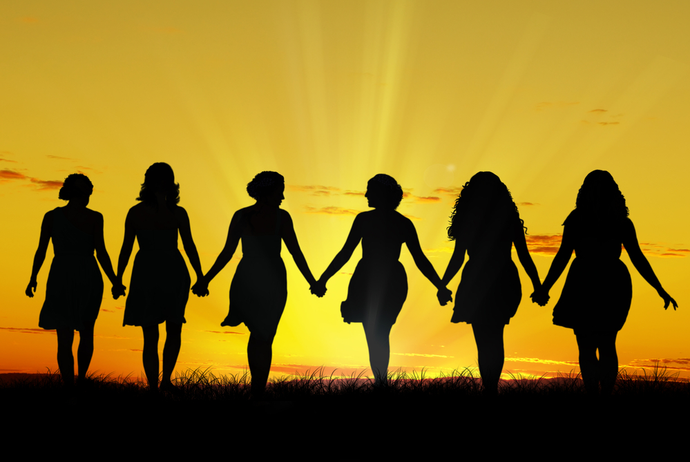 six women holding hands and walking toward the setting sun