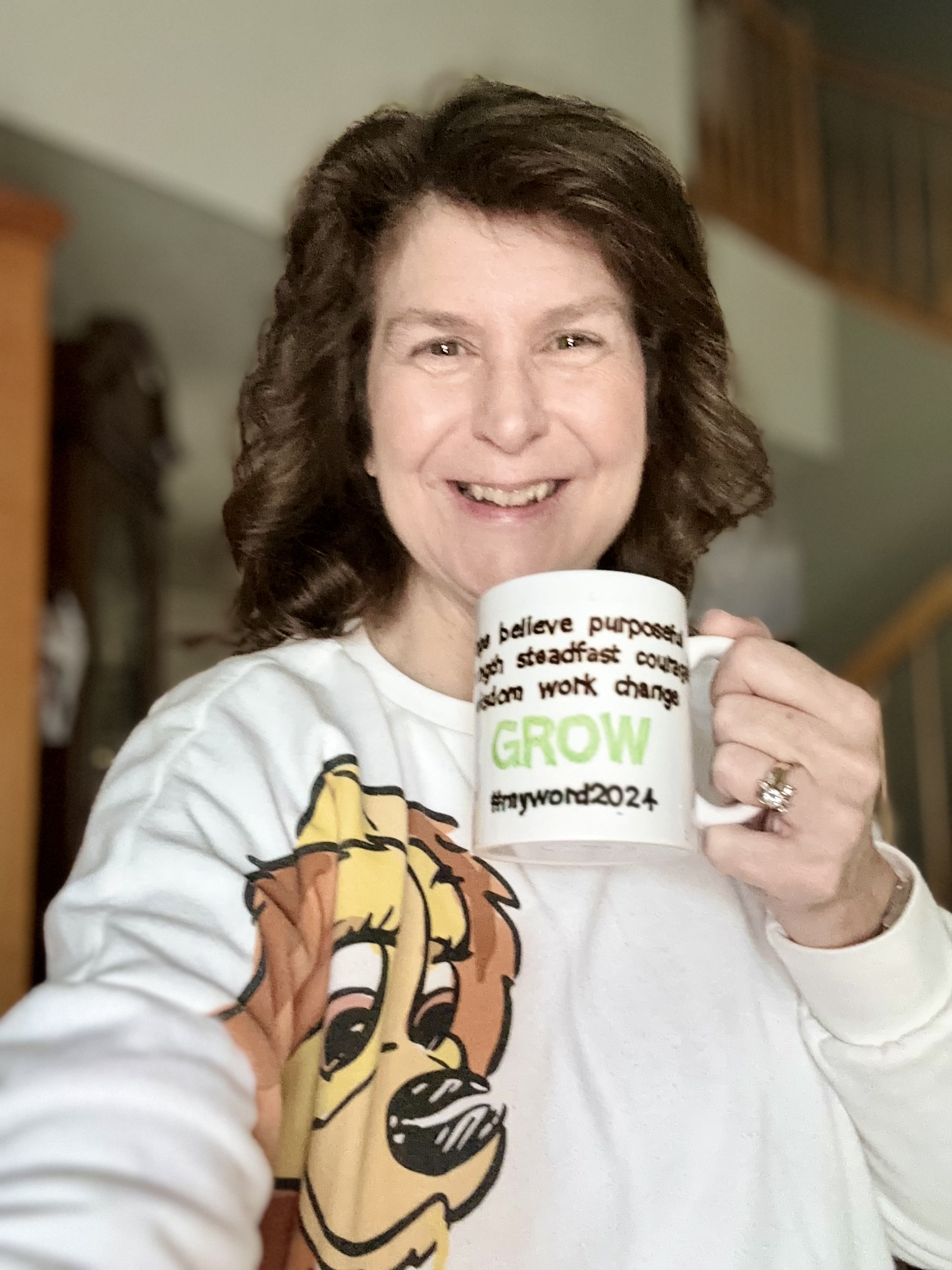 Denise M. Colby holding her handmade mug with all her words of the year on it with GROW, her 2024 word, the largest.